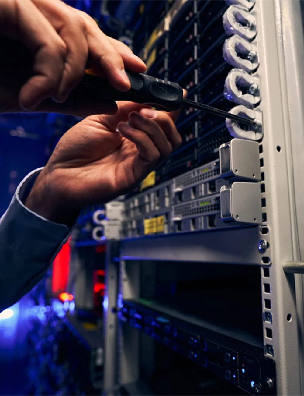 Close up of hands screwing in a screw with a screwdriver into a hole in a server rack.